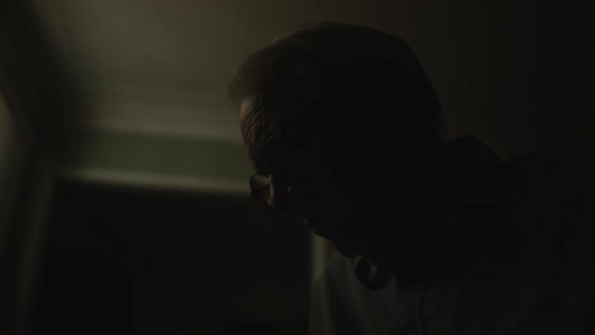 A man wearing glasses with a sad face in a dark room