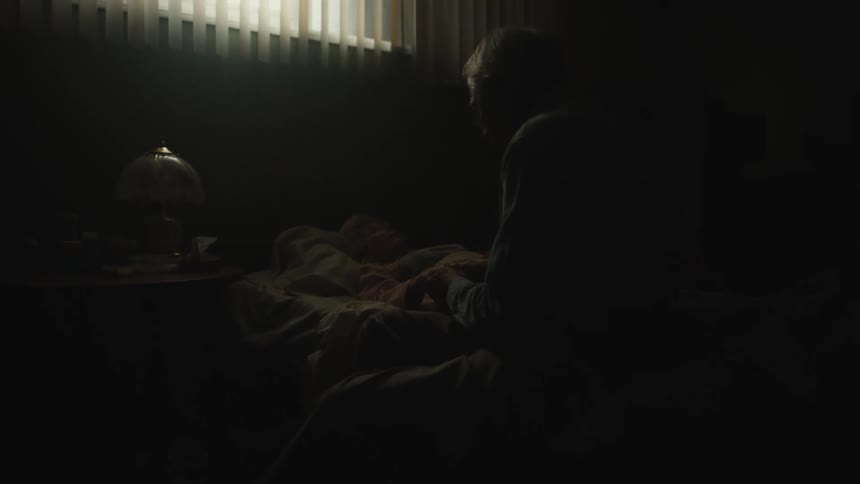 An old man sitting on the bedside of a sick old woman