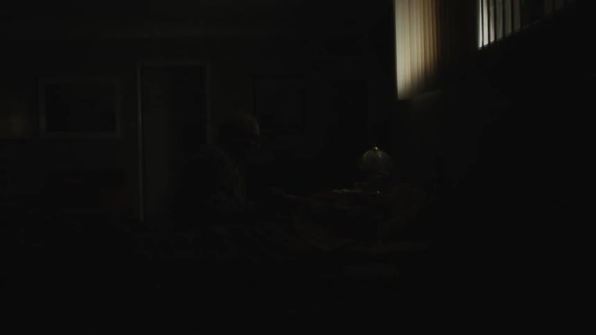 An elderly man is taking care of an elderly woman who is lying on the bed and they are holding hands