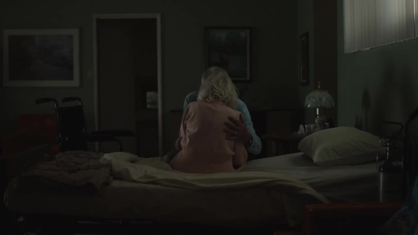 An elderly man helping an elderly woman to lie down