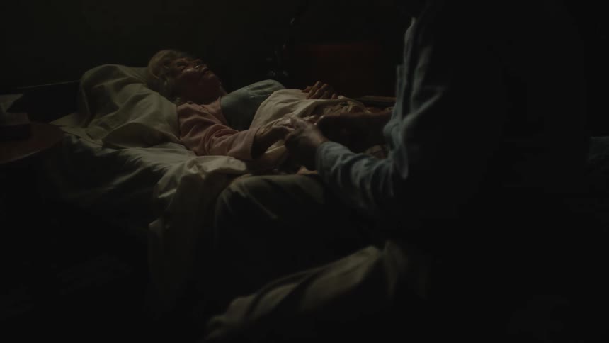 Man holds hand of elderly female invalid lying in bed