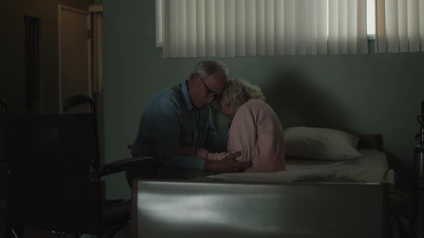 An elderly couple hugging each other sitting on the bed in their room