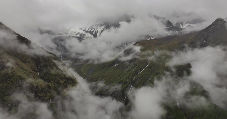A green valley under snowy mountain peaks and fog clouds