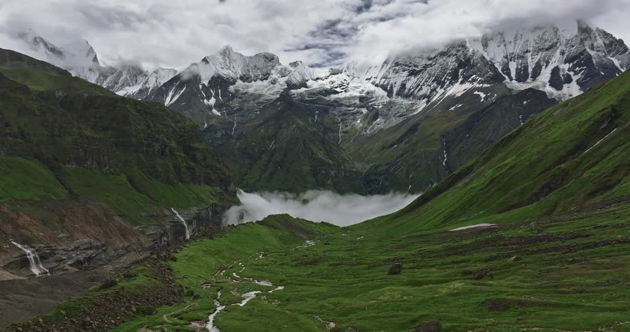 A green plateau under snowy mountain peaks and above a foggy valley