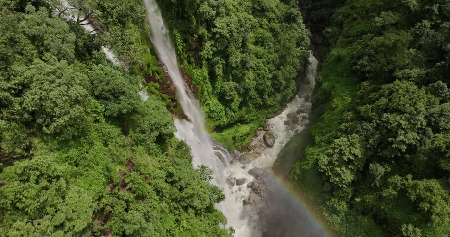 Water flows down waterfalls and along river through forest under a rainbow