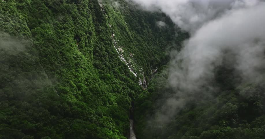 Aerial of a river between mountains and forest during a cloudy day