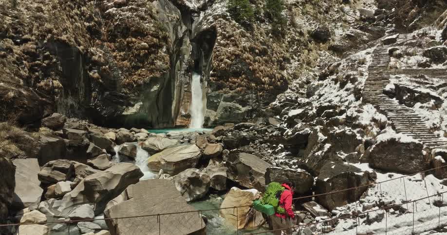 An aerial clip of a hiker crossing a bridge covered with ice