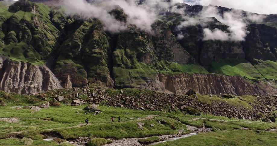 Three people walking on a dirt road in a region with mountains covered in grass and rocks
