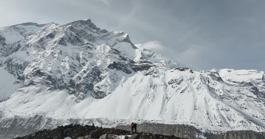 Landscape of two people on a peak with massive snowcovered mountains in the foreground