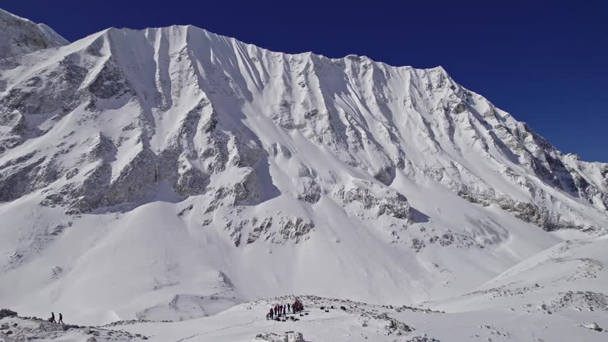 A group of hikers at the foot of a snowy mountain range