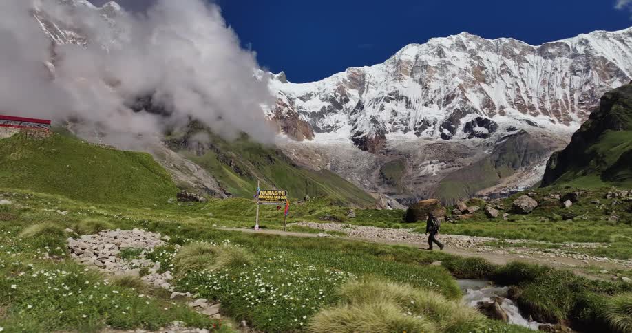 Person hikes past namaste sign in green valley near snow covered mountain
