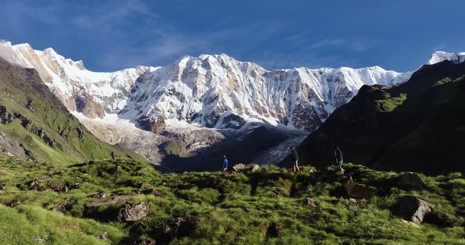 Three men walking on a mountain with vegetation and in the background a chain of snowcovered mountains