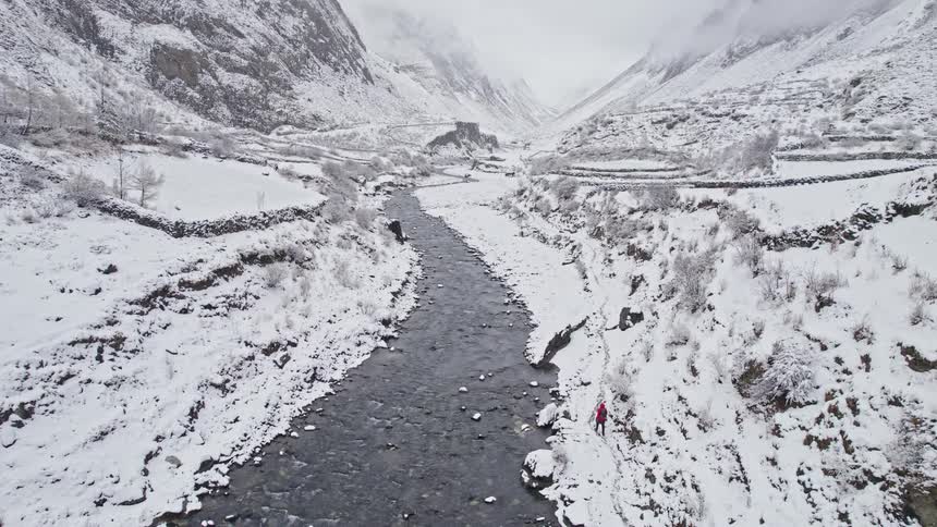 Aerial panorama of a person walking alongside a river amidst a chain of snowcovered mountains