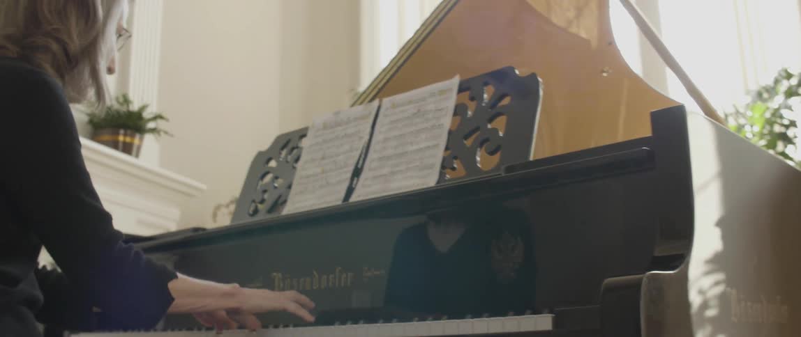 A woman is playing the piano with sun coming in from the window