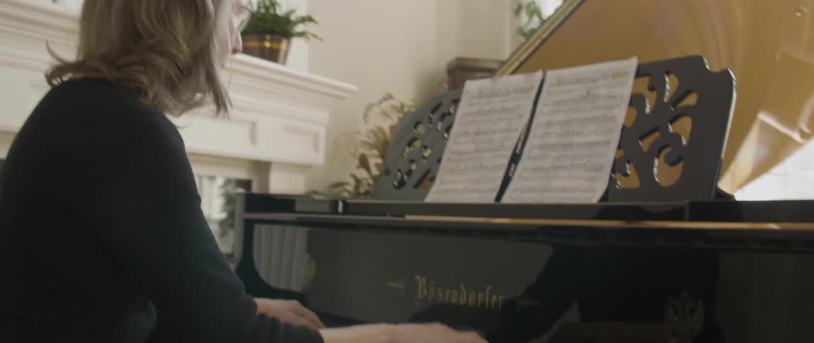 A woman wearing glasses plays the piano