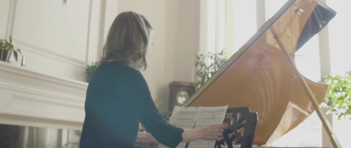 A woman walking to a piano and sitting at the bench