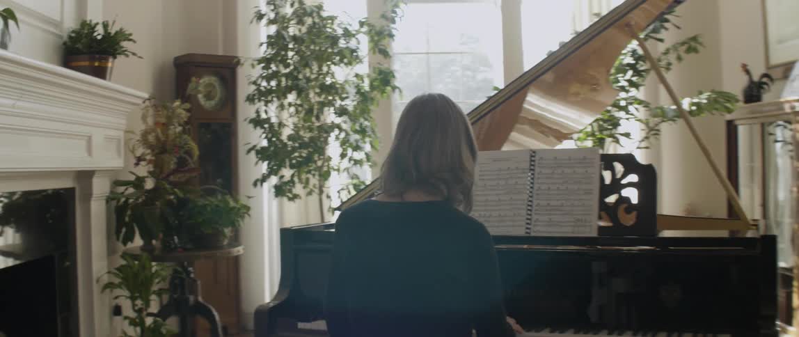 A woman is playing at a piano near a large window