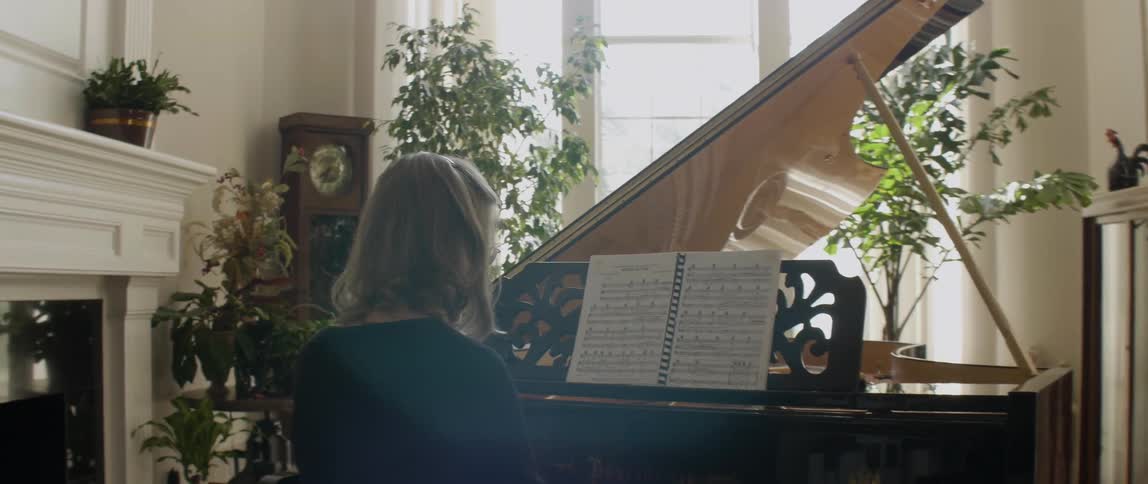 A woman is using sheet music as she plays the piano