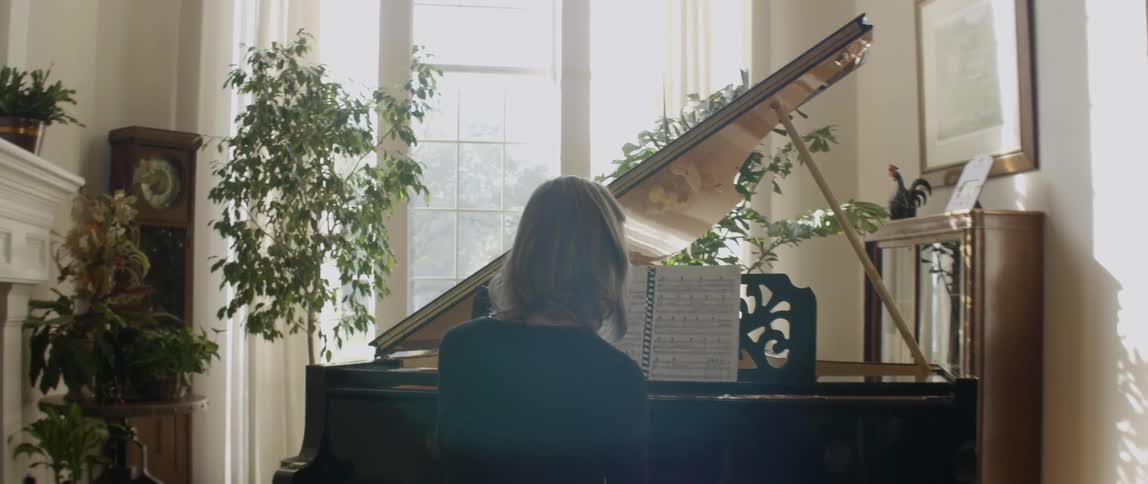 A woman is playing a piano in front of a large window