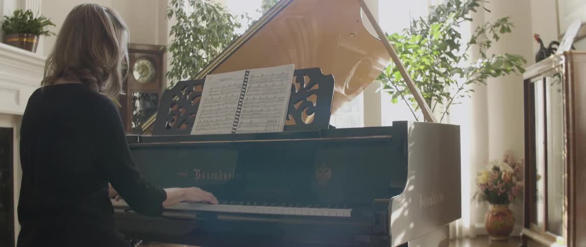 A woman moves from one to two hands playing a piano