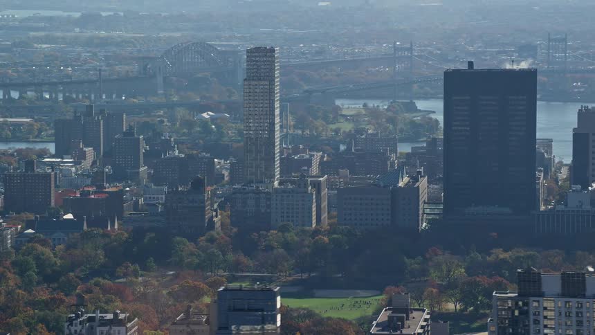 A city with tall buildings and behind it there is a river and a bridge that crosses it
