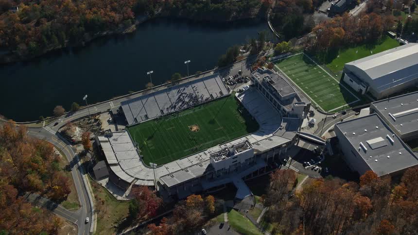 A stadium with cars parked in its car park and a road close by it next to a lake