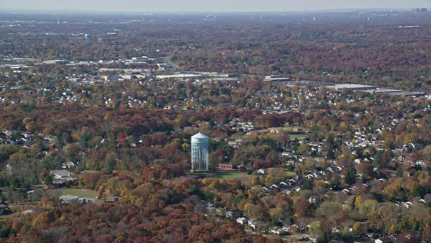 Aerial of a suburban area with a water tower and trees covered with changing leaves under an overcast sky