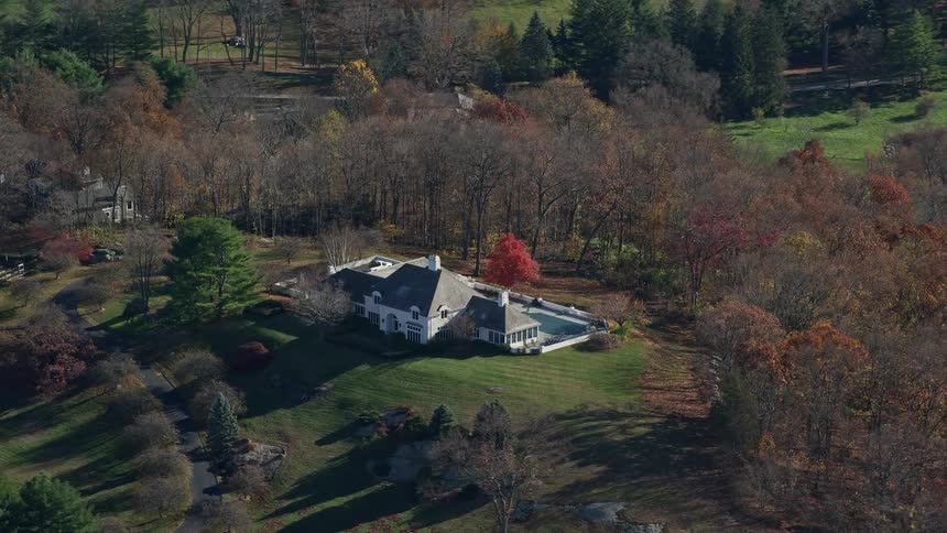 Aerial view of a mansion on a hill amidst nature with lawns and trees