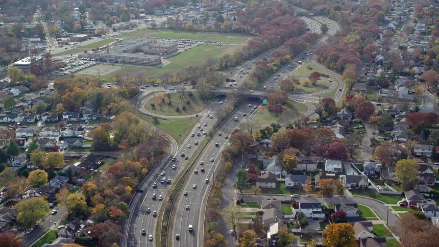A highway with many vehicles and on the sides there are suburbs with many residential buildings