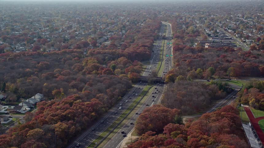 A double lane busy highway surrounded by trees passing through a sub urban town