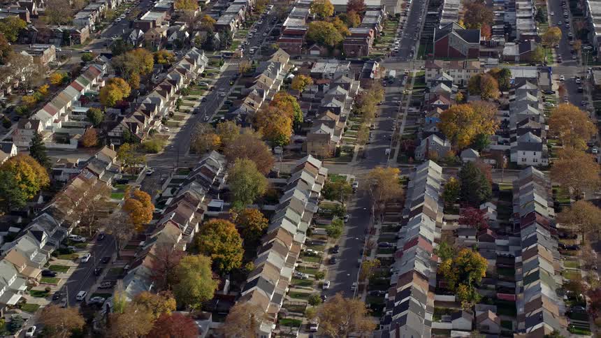 Aerial view of neighborhoods with houses close together as cars travel on the streets with trees in fall colors