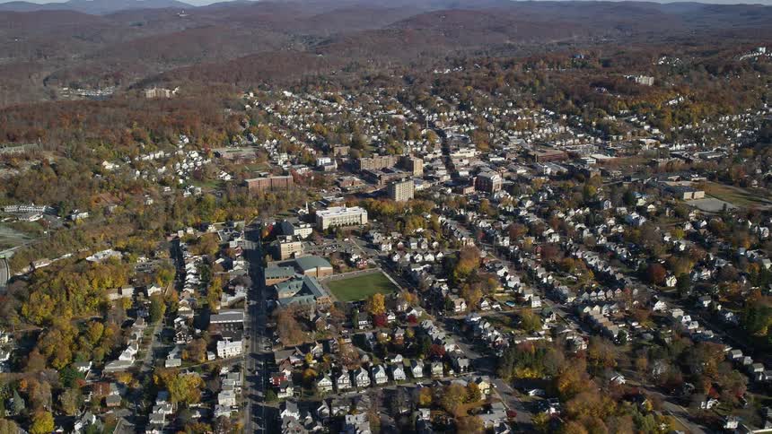 Aerial of wooded town bordering hills during the fall
