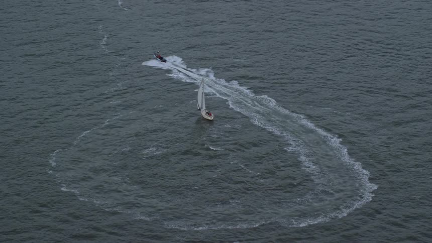 Aerial view of speed boat wake near sailboat in open water