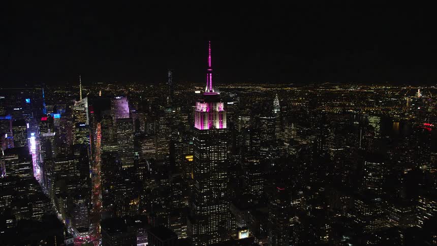 A metropolitan city at night with huge buildings and one of them has a pink light on top