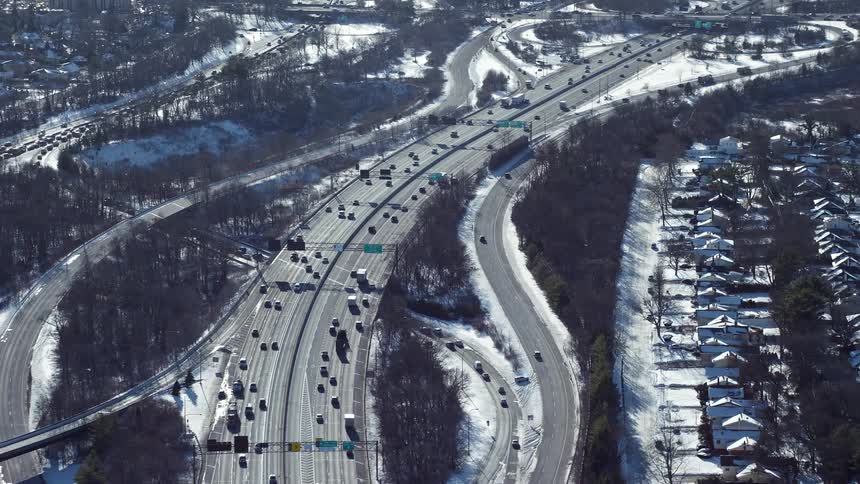 Aerial panorama of a highway next to a residential neighborhood during winter with snow