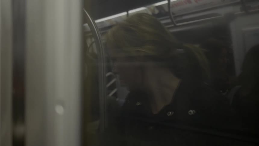 A woman's reflection is in the window of a moving train