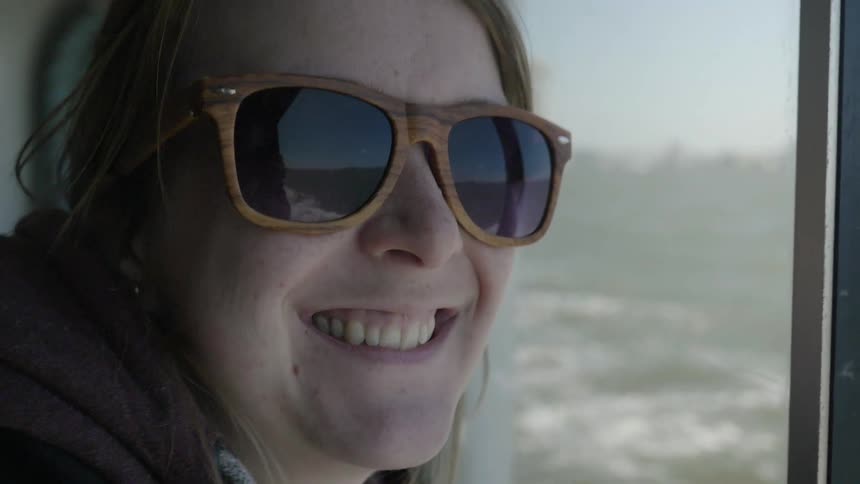 A woman with sunglasses smiles as she looks out a window