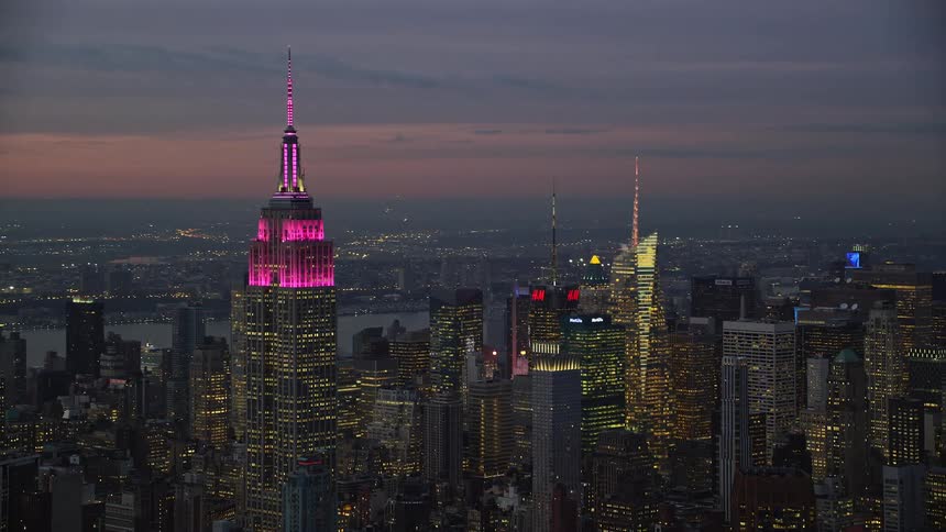 Aerial panorama of a tower with pink lights and skyscrapers by the seaside under a purple dawn sky