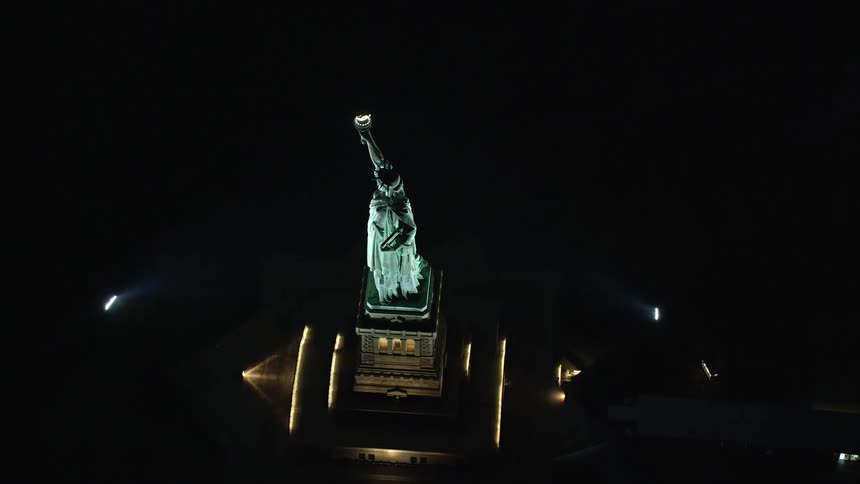 Light shines on the statue of liberty as she stands tall in the darkness