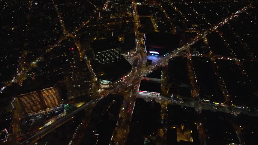 Aerial panorama of a nighttime metropolis with a central events venue amidst a highway