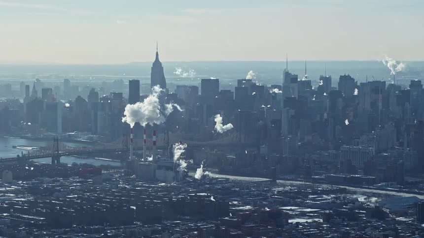 Aerial view of skyscrapers in a metropolis by the seaside with factories emitting smoke