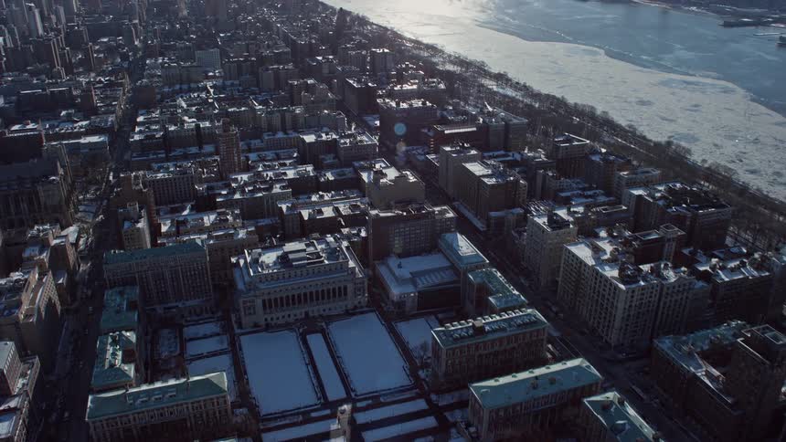 Traffic moves along city streets paralleling frozen river with downtown skyline in the distance