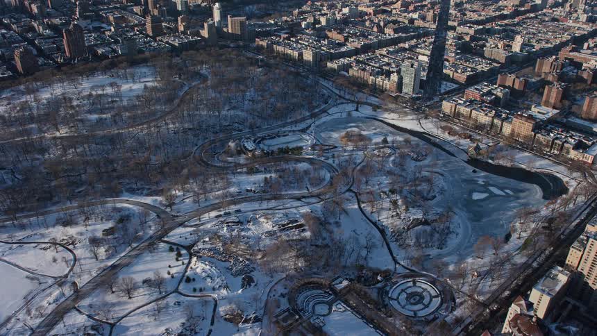 Aerial view of a central park covered in snow in the midst of a metropolis