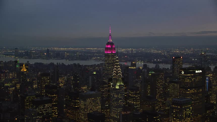 Skyline of the empire state building lit up in pink during dusk