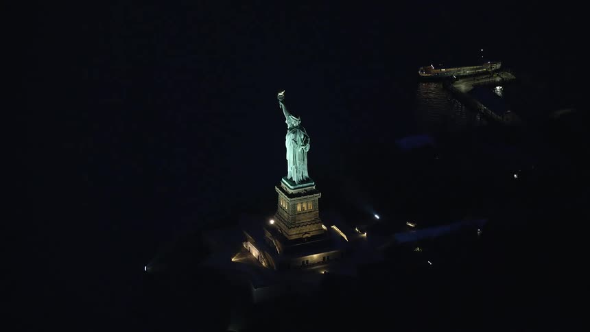 The statue of liberty holds her torch high as she overlooks new york harbor in the darkness