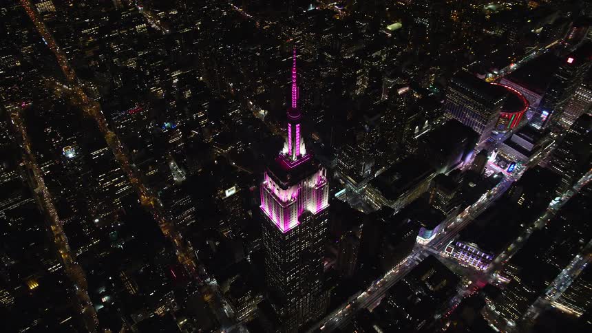 Skyscraper with pink lights on upper stories towers over city scape at night