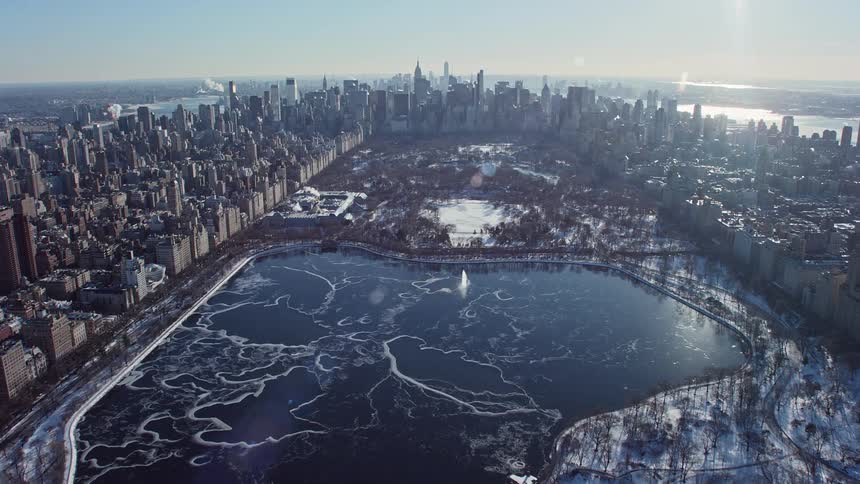 Aerial panorama of a snowy park with a lake in a metropolitan city under a dawn sky