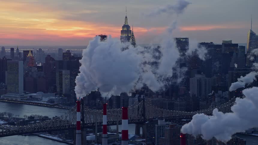 Aerial view of factory smoke with a metropolitan city by the seaside in the background and a red morning sky