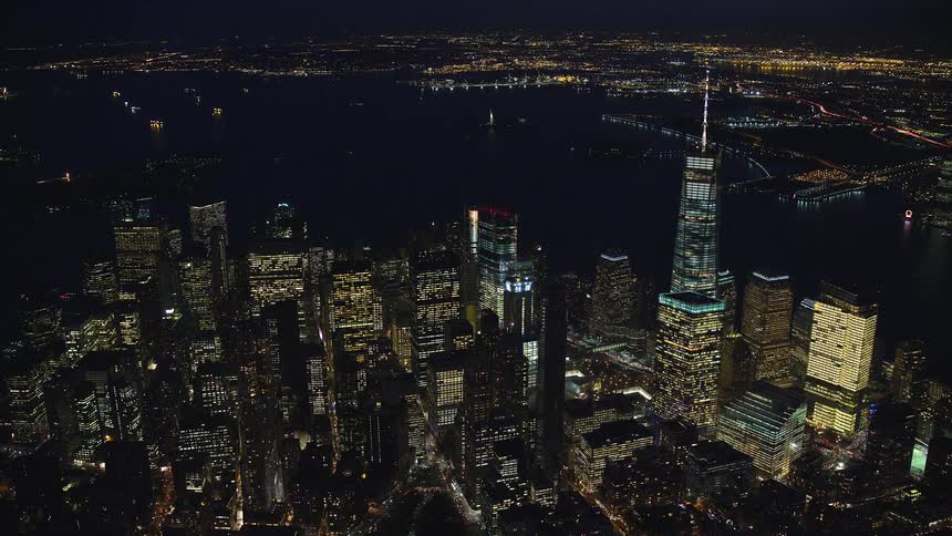 Aerial of one world trade center towering over new york city skyscrapers near waterfront at night
