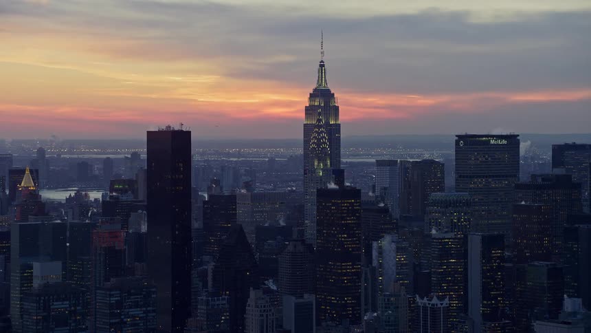 A metropolitan city with a huge tower and in the sky there is an orange sunlight